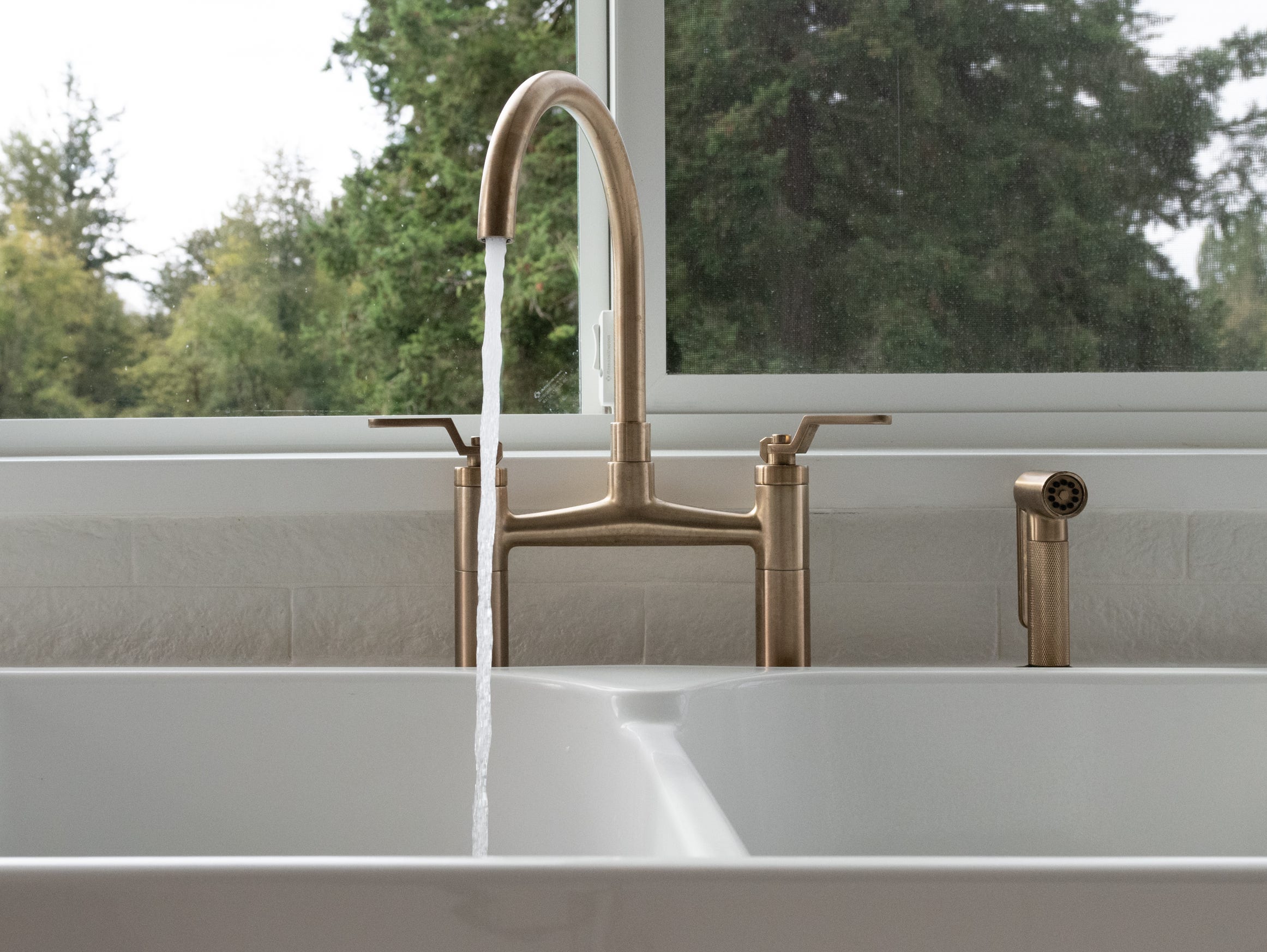 Gold water faucet in the kitchen of a modern, brightly lit suburban upscale farmhouse.